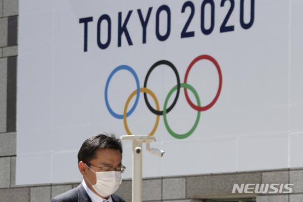 25일(현지시간) 일본 도쿄도청에 걸린 2020 도쿄올림픽 로고 앞을 한 행인이 마스크를 쓰고 걸어가고 있다. 오는 7월 예정돼 있던 도쿄올림픽은 신종 코로나바이러스 감염증(코로나19) 여파로 내년으로 연기됐다. 2020.3.25.